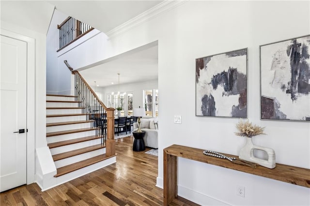 foyer entrance with stairway, a notable chandelier, ornamental molding, and wood finished floors