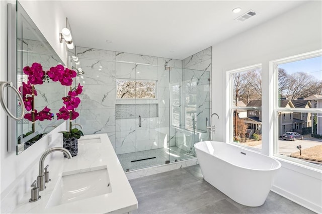 bathroom featuring a marble finish shower, double vanity, visible vents, a freestanding bath, and a sink