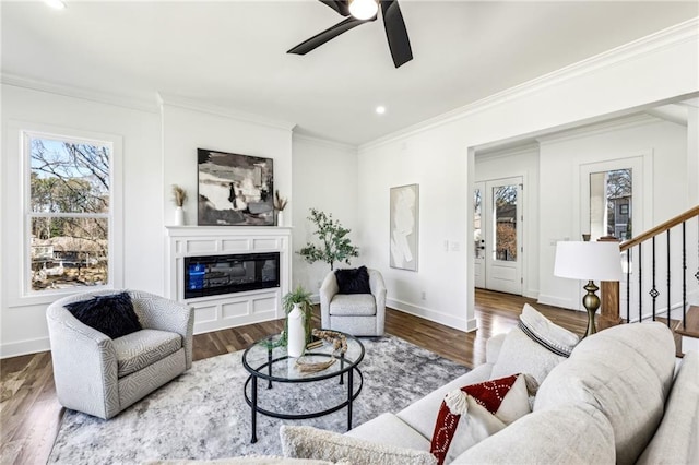 living room with baseboards, wood finished floors, a glass covered fireplace, and crown molding