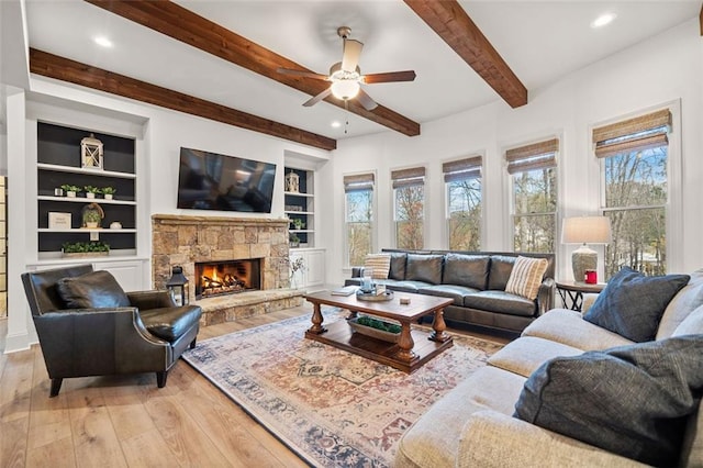 living room featuring light hardwood / wood-style flooring, ceiling fan, built in features, a fireplace, and beamed ceiling