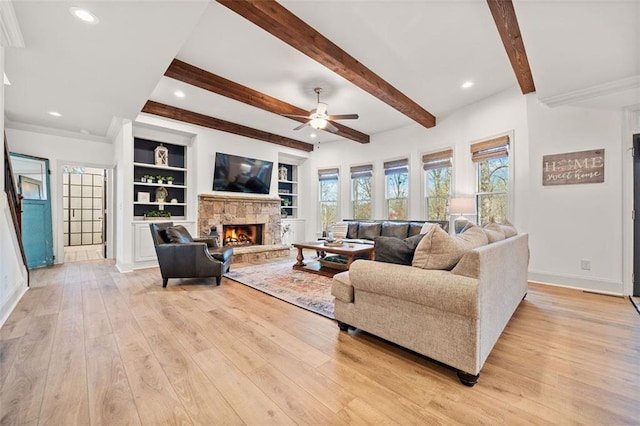 living room with ceiling fan, light hardwood / wood-style floors, a stone fireplace, and beam ceiling