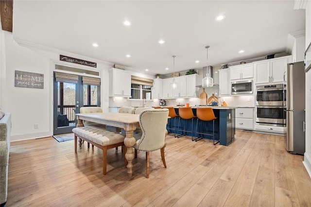 kitchen featuring wall chimney exhaust hood, a kitchen breakfast bar, decorative light fixtures, a kitchen island, and appliances with stainless steel finishes