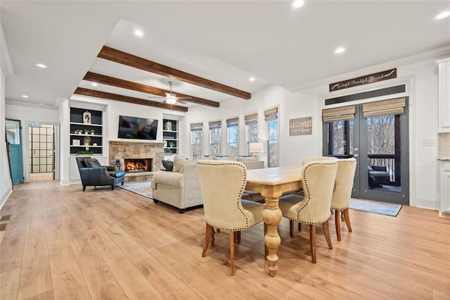 dining space featuring light hardwood / wood-style flooring, ceiling fan, built in shelves, a fireplace, and beam ceiling