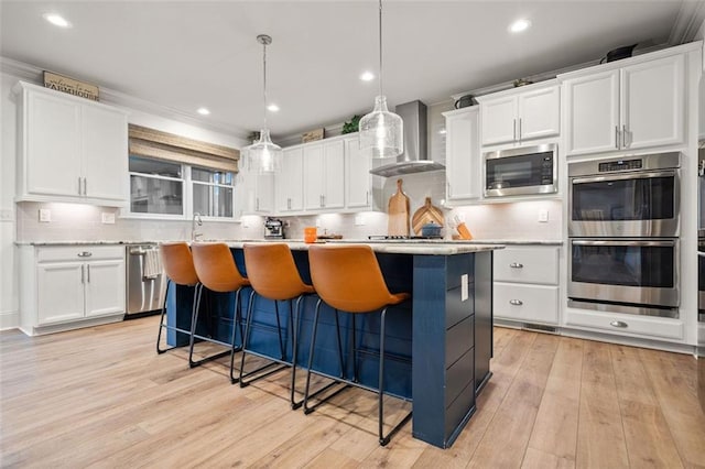 kitchen with white cabinets, decorative light fixtures, stainless steel appliances, and wall chimney range hood