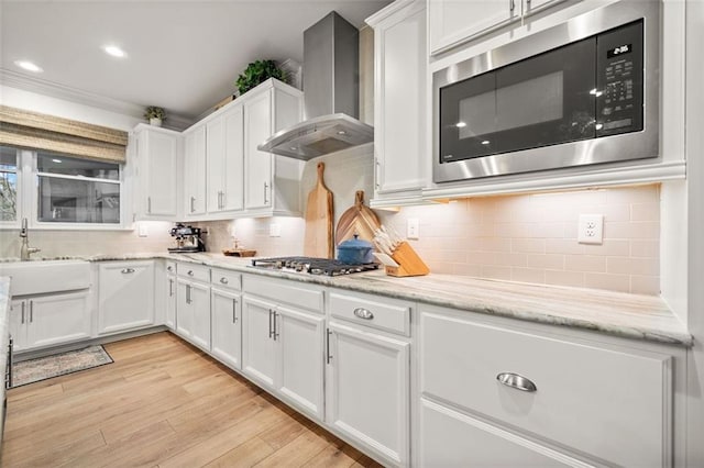 kitchen with appliances with stainless steel finishes, sink, wall chimney range hood, white cabinets, and light hardwood / wood-style floors