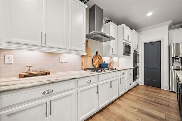 kitchen with appliances with stainless steel finishes, light wood-type flooring, ornamental molding, wall chimney range hood, and white cabinets