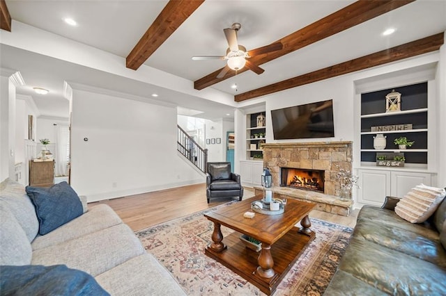 living room with built in shelves, ceiling fan, beam ceiling, a fireplace, and light hardwood / wood-style floors