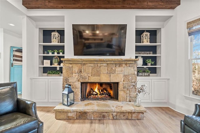 living room with built in shelves, crown molding, a fireplace, and light hardwood / wood-style floors