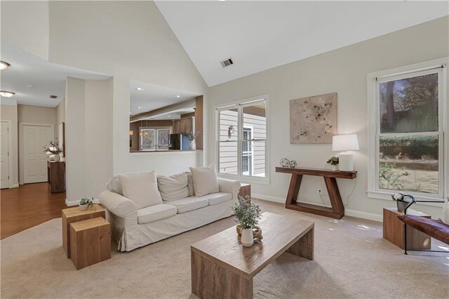 sitting room featuring plenty of natural light, high vaulted ceiling, and light carpet