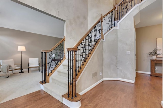 staircase with wood-type flooring and a towering ceiling