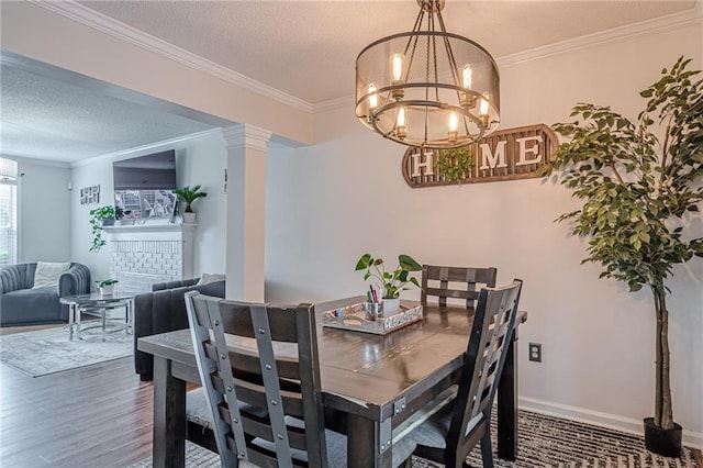 dining space featuring a chandelier, a textured ceiling, wood finished floors, crown molding, and ornate columns