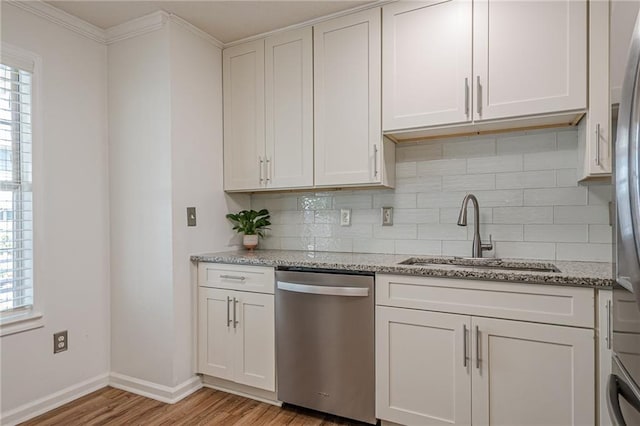 kitchen featuring dishwasher, a sink, light wood finished floors, backsplash, and baseboards