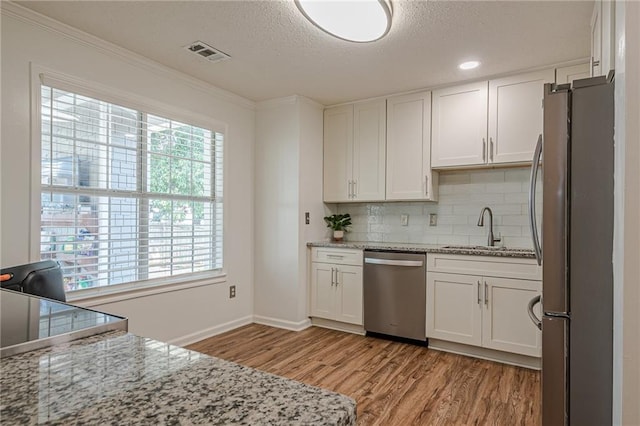 kitchen featuring stainless steel appliances, a sink, light wood-style flooring, white cabinets, and baseboards