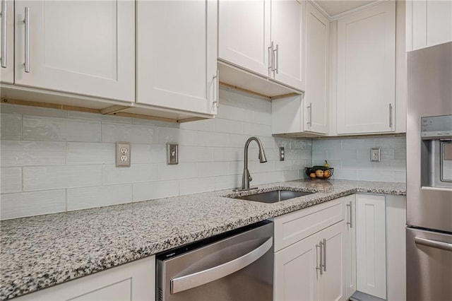 kitchen featuring stainless steel appliances, a sink, white cabinetry, decorative backsplash, and light stone counters