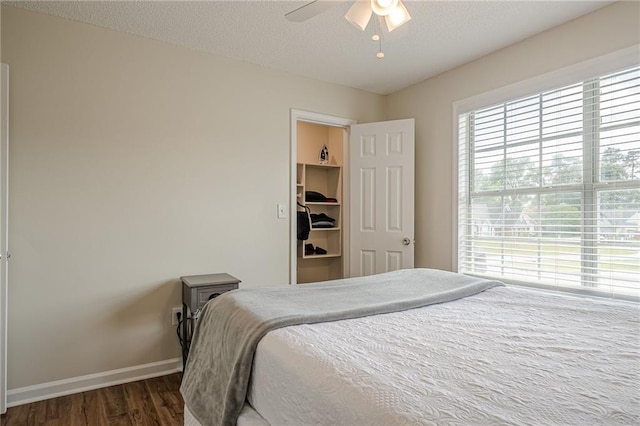 bedroom with dark wood-style flooring, baseboards, a textured ceiling, a spacious closet, and ceiling fan