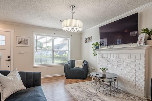living area with wood finished floors, ornamental molding, a textured ceiling, a chandelier, and baseboards
