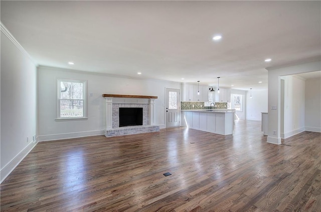 unfurnished living room with baseboards, ornamental molding, dark wood-style flooring, a brick fireplace, and recessed lighting