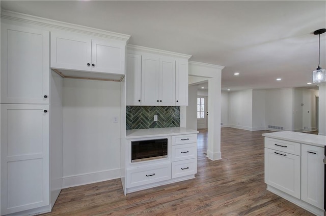 kitchen with built in microwave, white cabinetry, backsplash, and wood finished floors