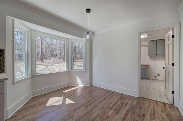 unfurnished dining area featuring baseboards, ornamental molding, and wood finished floors