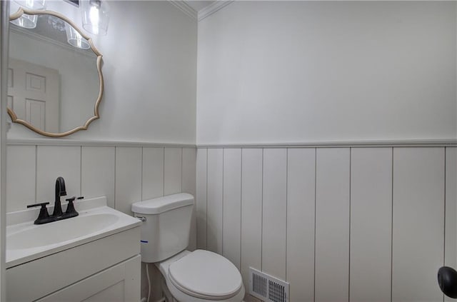 half bath with visible vents, toilet, ornamental molding, wainscoting, and vanity