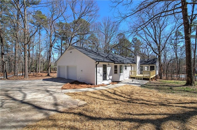 view of home's exterior with a deck, a garage, driveway, a lawn, and a chimney