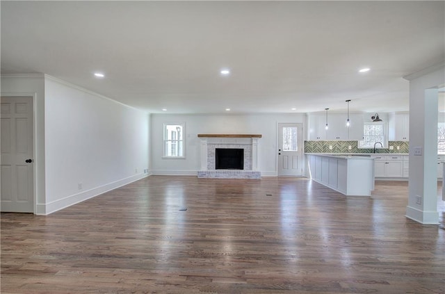 unfurnished living room featuring recessed lighting, dark wood-style flooring, a brick fireplace, and baseboards