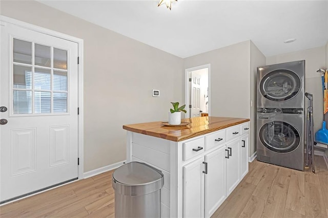 clothes washing area featuring stacked washer and dryer, cabinets, and light hardwood / wood-style floors