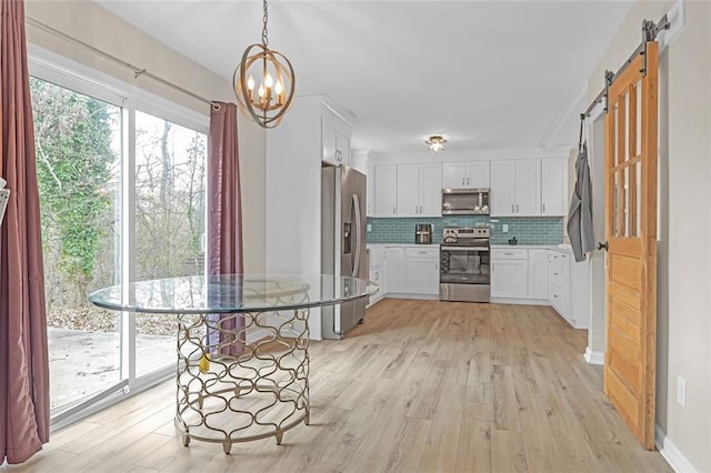 kitchen featuring white cabinetry, hanging light fixtures, stainless steel appliances, decorative backsplash, and a barn door