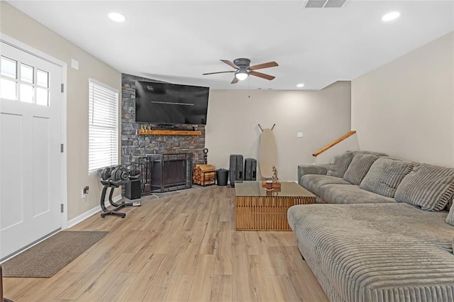 living room featuring ceiling fan, a stone fireplace, and light wood-type flooring