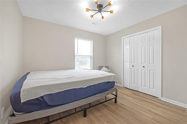 bedroom with a closet, a textured ceiling, light hardwood / wood-style flooring, and a notable chandelier