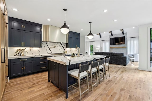 kitchen with wall chimney exhaust hood, a kitchen bar, backsplash, light wood-style floors, and a sink