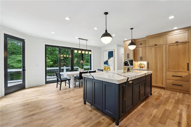 kitchen with light wood-type flooring, pendant lighting, recessed lighting, light stone counters, and a center island with sink