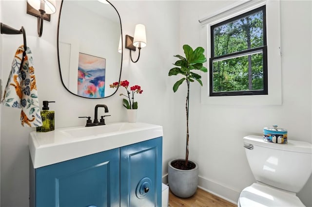 half bath featuring toilet, vanity, wood finished floors, and baseboards