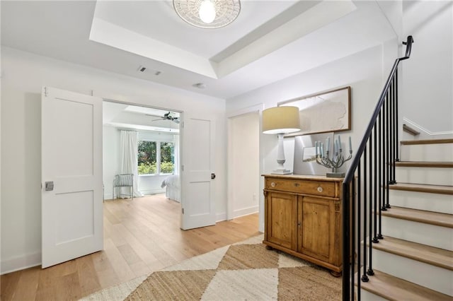 foyer entrance featuring light wood-style floors, a raised ceiling, stairs, baseboards, and a ceiling fan