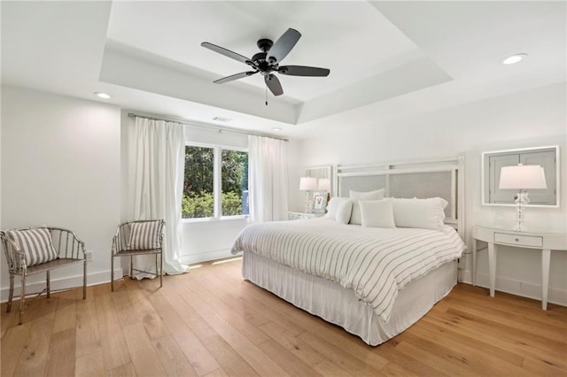bedroom with a tray ceiling, light wood-style floors, baseboards, recessed lighting, and ceiling fan
