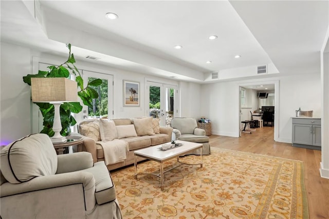 living area featuring a raised ceiling, light wood-type flooring, and recessed lighting