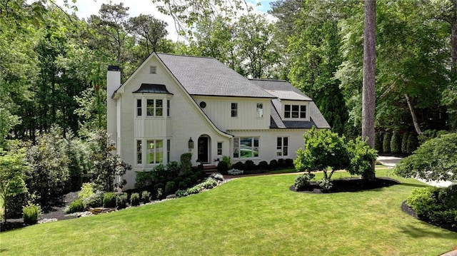 french provincial home featuring a chimney, a front lawn, and view of wooded area