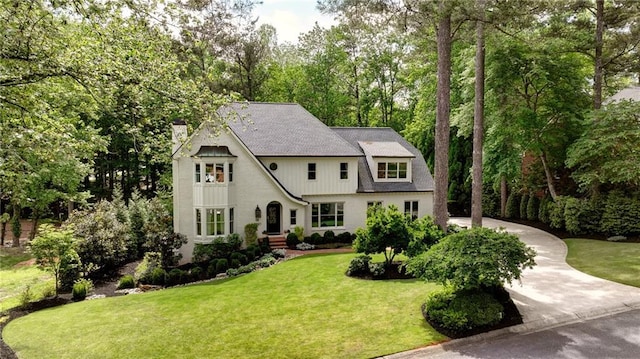 view of front facade featuring a front yard, driveway, a chimney, and view of wooded area