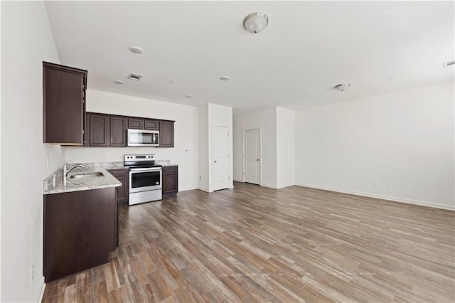 kitchen with hardwood / wood-style flooring, appliances with stainless steel finishes, dark brown cabinets, light stone counters, and sink