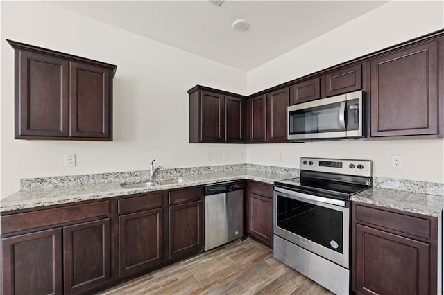 kitchen featuring appliances with stainless steel finishes, light wood-type flooring, dark brown cabinets, light stone countertops, and sink