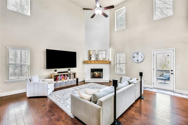 living room featuring a towering ceiling, ceiling fan, plenty of natural light, and dark wood-type flooring