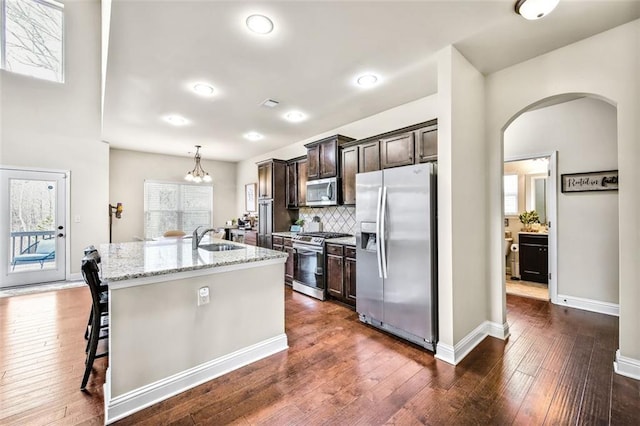 kitchen featuring light stone countertops, a kitchen breakfast bar, stainless steel appliances, a kitchen island with sink, and dark brown cabinets