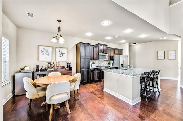 kitchen featuring decorative light fixtures, decorative backsplash, light stone countertops, a center island with sink, and appliances with stainless steel finishes