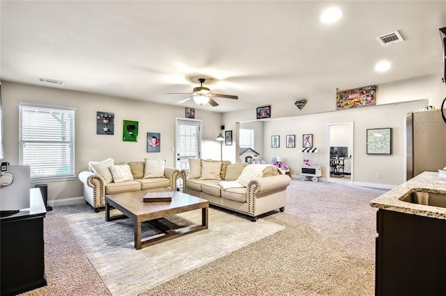 living room featuring sink, light colored carpet, ceiling fan, and plenty of natural light