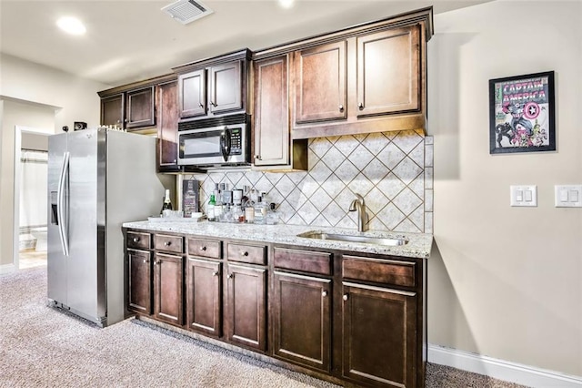 kitchen with stainless steel appliances, light stone counters, sink, dark brown cabinets, and backsplash