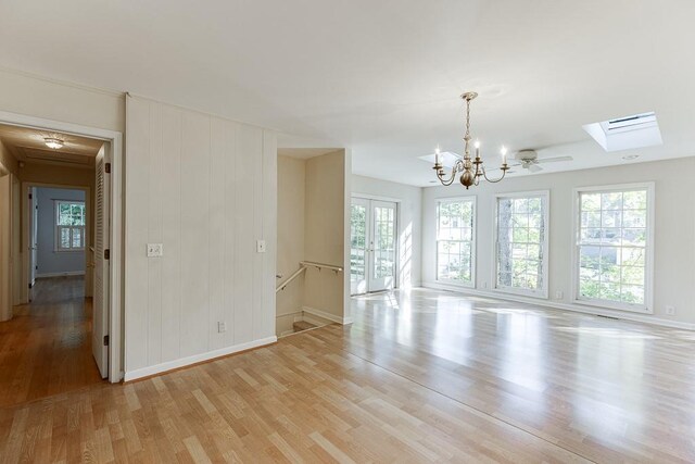 unfurnished room with a skylight, light wood-type flooring, and ceiling fan with notable chandelier