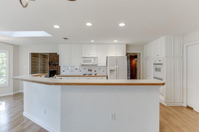 kitchen with a spacious island, white appliances, white cabinets, light hardwood / wood-style floors, and a skylight