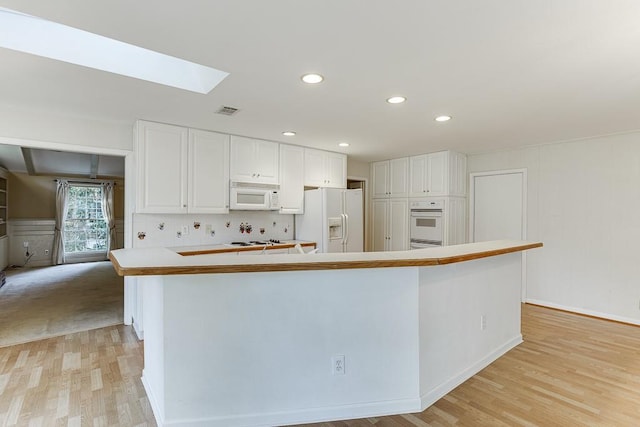 kitchen with white appliances, a skylight, a kitchen island, white cabinetry, and light hardwood / wood-style floors