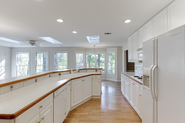 kitchen with white cabinets, a skylight, light hardwood / wood-style floors, sink, and white appliances