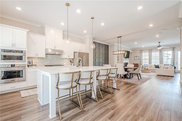 5005 Shay Town Ln, Peachtree Corners, GA 30092 - kitchen featuring decorative backsplash, an island with sink, light countertops, under cabinet range hood, and appliances with stainless steel finishes